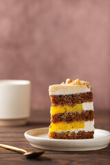 Piece of pumpkin or carrot layered cake with coconut cream, walnut and orange confit in a plate with cup of tea. Sugar, gluten and lactose free. Vertical orientation.