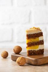 Piece of pumpkin or carrot cake with coconut cream, walnut and orange confit in a wooden board. Sugar, gluten and lactose free. Vegan, healthy dessert. Vertical orientation.