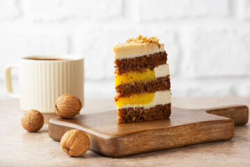 Piece of pumpkin or carrot cake with coconut cream, walnut and orange confit in a wooden board with cup of tea on a table. Sugar, gluten and lactose free. Vegan, healthy dessert.