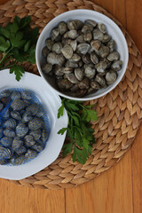 Many littleneck fresh clams in a white bowl with parsley leaves on wooden table