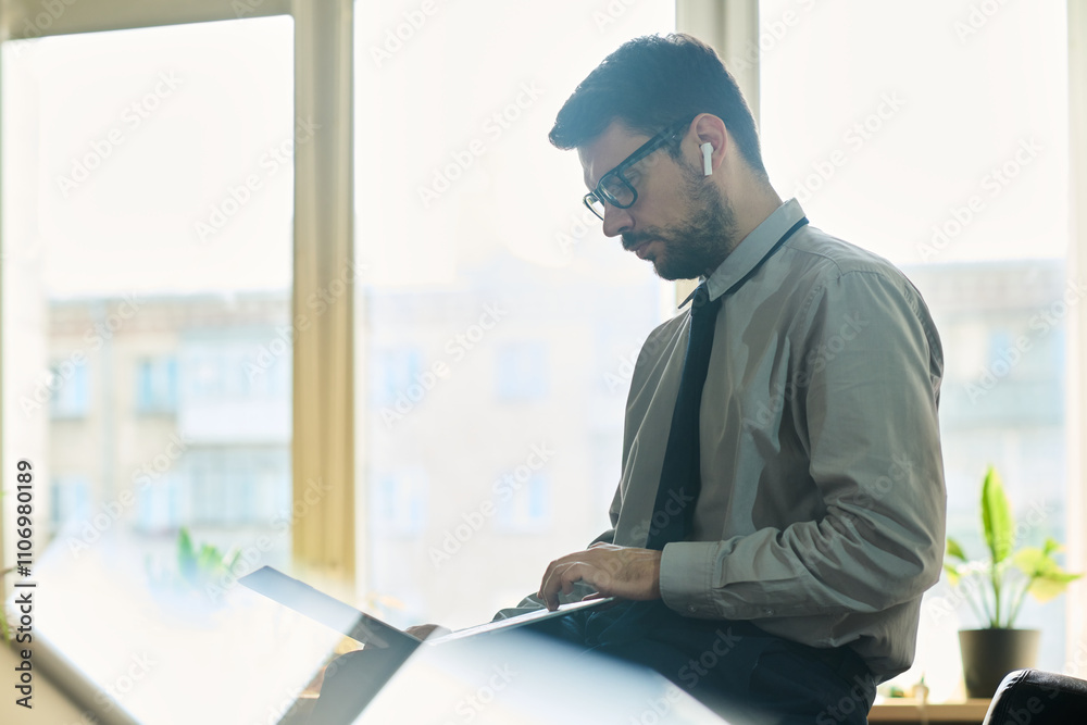 Poster side view of young confident market analyst sitting in front of camera in office and looking through