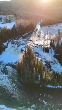 A tranquil winter river winds gracefully through a pristine Swedish forest blanketed in snow. The warm golden hues of sunrise illuminate the icy landscape.