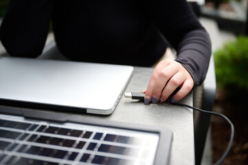 Female using portable solar panel to charge laptop and smartphone. Closeup view of a girl plugging...