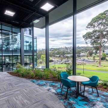 Modern office interior with panoramic windows, teal chairs, and small garden area.