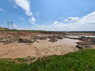 Construction activity is evident at a site with large dirt mounds and a water-filled pit on a sunny day