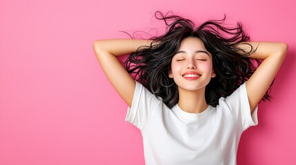 Fototapeta premium A young woman with curly hair smiles contentedly against a pink background, exuding joy and relaxation.