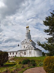 Fototapeta premium A stunning church features golden domes and intricate architecture surrounded by lush greenery under a cloudy sky