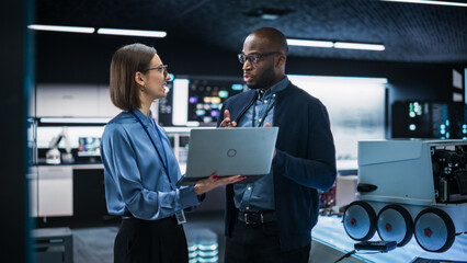 Portrait of a Team of Two Engineers Collaborating on Developing a Robot for Deliveries in a Manufacturing Facility. Colleagues Analysing Data Using Laptop Computer and Brainstorming for a Project