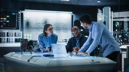 Diverse Group of Industrial Robotics Specialists Gathered Around a Table, Using Laptop Computer to...
