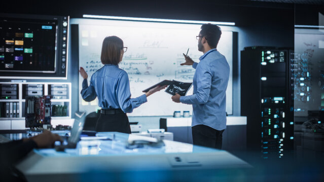 In Technological Research Facility: Portrait of a Team of Two Professional Engineers Using Digital Tablet and White Board to Discuss the Manufacturing Plan for Product Development