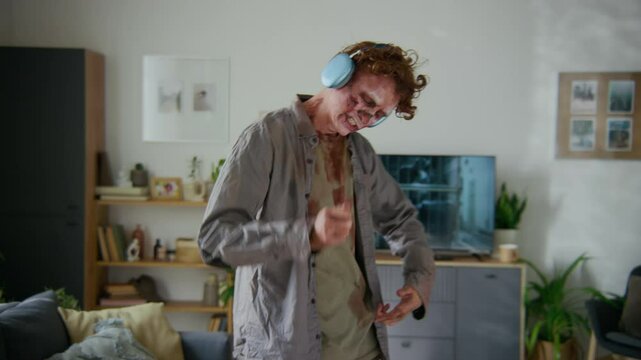 Medium full shot of male walking dead in bloody clothes, wearing wireless headphones, enjoying music in its particular way, rocking to beat with jerky, jolting movements, then pretending to sing along