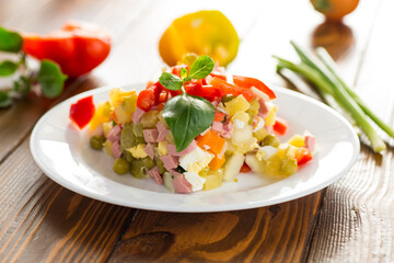 vegetable salad of boiled vegetables, with peas, sausage, sweet pepper. On a wooden table