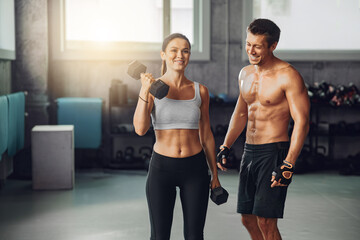 A fit couple exercising with dumbbells in a vibrant gym, showcasing fitness and teamwork through dedication