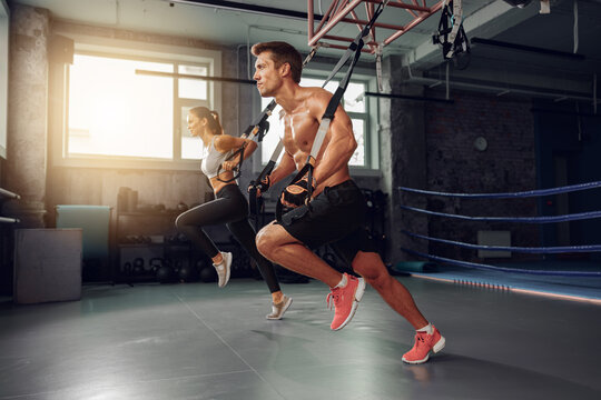 Two individuals engage in intense TRX training, showcasing strength and fitness in a modern gym setting.