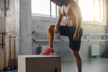 A fit man is diligently performing an intense workout routine on a sturdy box within a modern gym...