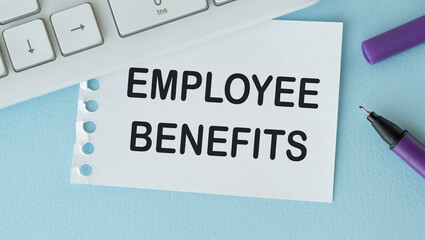EMPLOYEE BENEFITS text on a notebook with keyboard , pen glasses on white blue background.