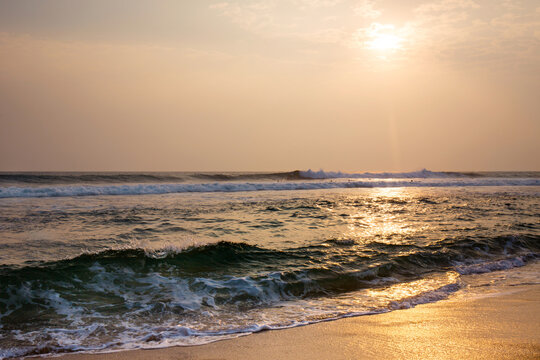 The ocean is calm and the sun is setting, surfers with boards are riding the waves - Powered by Adobe