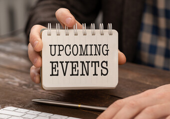 Text Upcoming Events written in notepad, Office desk with electronic devices, computer and paper, wood table from above, concept image for blog title or header image.