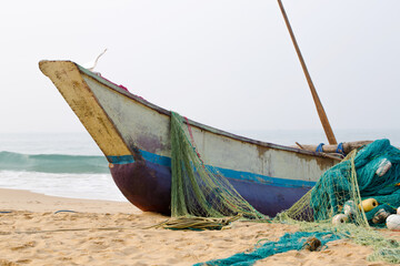 A fishing boat stands on the shore near the ocean, a green net with large floats lies next to it