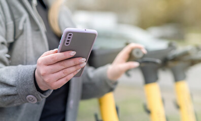 Young Woman Unlocks an e-scooter with her mobile phone, modern transport in big city
