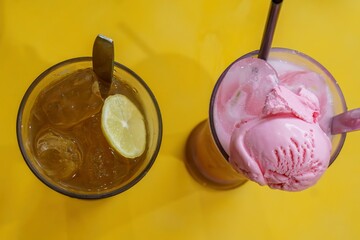 A refreshing glass of iced lemon tea with a spoon handle and a delectable strawberry milkshake