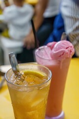 A refreshing glass of iced lemon tea with a spoon handle and a delectable strawberry milkshake