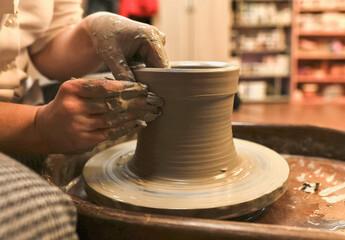 clay potter artist making pot shape on wheel pedestal.