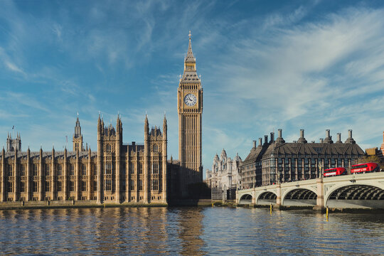 Big ben clock tower and houses of parliament are reflecting on thames river on a sunny day with blue sky and some clouds in london, united kingdom