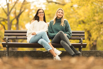 Two beautilful young women sitting on the bench in publiic park