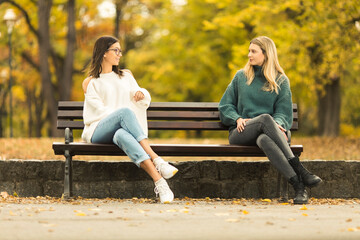 Two beautilful young women sitting on the bench in publiic park