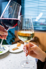 Two glasses clink together in a toast, one filled with red wine and the other with white wine. The setting features a modern ambiance with soft lighting and a blurred background.