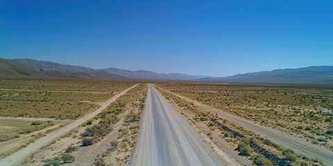 Naklejka premium A long, empty road stretching through a desert landscape under a clear blue sky.