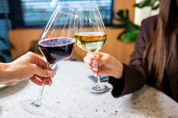 Two elegant wine glasses clink together in celebration, one filled with red wine and the other with white. The setting features modern decor and greenery, suggesting a stylish gathering.