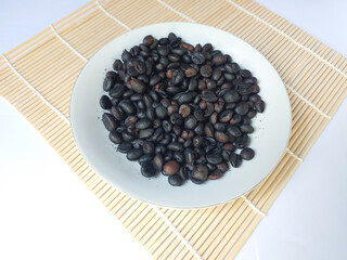 Roasted coffee beans on a white plate on bamboo mat with white background