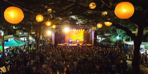 A bustling outdoor concert at night with a glowing stage, cheering crowd, and vibrant light effects. The energetic atmosphere is full of excitement and celebration.