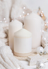 Pillar candles with label near white sweater and Christmas decor and lights, holiday mockup