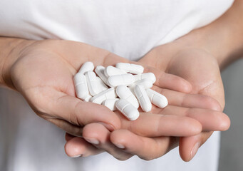 Cupped womans hands with a pile of mixed white medical pills closeup over white shirt