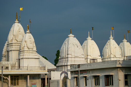 A magnificent white temple with intricate domes and golden spires, adorned with yellow flags, standing against a clear blue sky.The serene structure of jain temples in Hastinapur, uttar pradesh india.