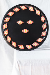 A colorful face-like arrangement of ceramic khachapuri magnets on a black tray, showcasing the vibrant design of this traditional Georgian food art