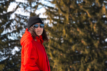 Young woman in red jacket in snowy mountains in a sunny day. Landscape with beautiful girl on the hill in snow forest.