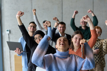 A diverse team of business professionals ecstatically celebrating their success in a modern office,...