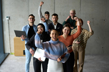 A diverse team of business professionals ecstatically celebrating their success in a modern office,...