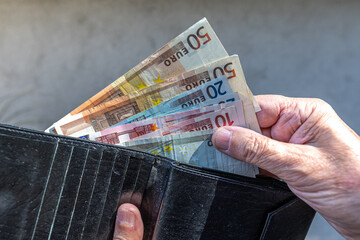 Close-up of a fan of Euro banknotes held on a person's hand, being pulled from a black wallet. The denominations go from 5 to 50 Euros, and illuminated by the sun with a pattern of shadows.