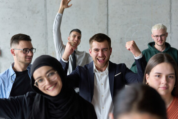 A diverse team of business professionals ecstatically celebrating their success in a modern office,...