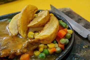 Close-up of crispy golden french fries with colorful roasted vegetables including carrots, corn, and green beans, drizzled with a rich and savory chicken steak sauce.
