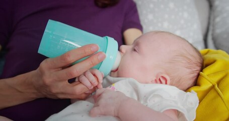 Mother feeding her infant baby with milk baby bottle at home, portrait infant Baby eating, drinking formula feeding. Concept of healthy eating, artificial nutrition, infant feeding