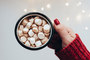 Woman holds Christmas cup of cocoa with with lights bokeh on a white background.