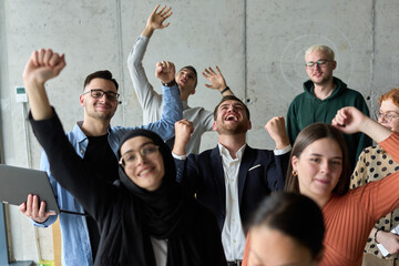 A diverse team of business professionals ecstatically celebrating their success in a modern office,...