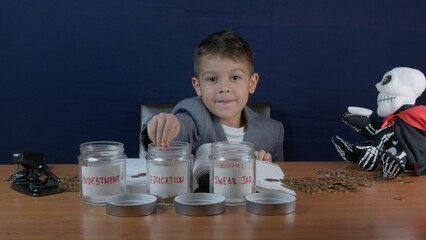 Child in a busiess suit with sceptic face expression putting coins in a jar for Education savings. High quality photo