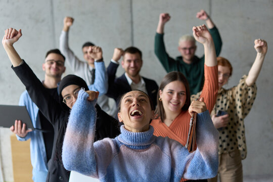 A diverse team of business professionals ecstatically celebrating their success in a modern office, expressing triumph and unity after achieving their goals